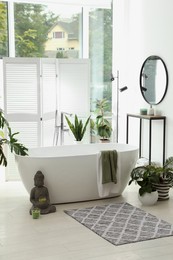 Photo of Stylish bathroom interior with modern tub, window and beautiful houseplants. Home design