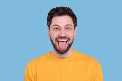 Photo of Happy man showing his tongue on light blue background