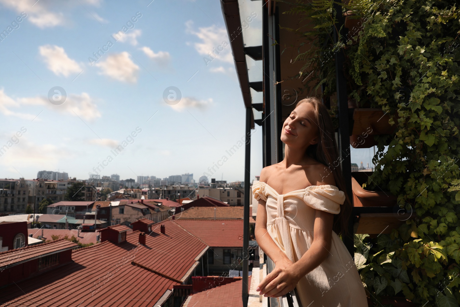 Photo of Beautiful young woman standing on balcony, space for text