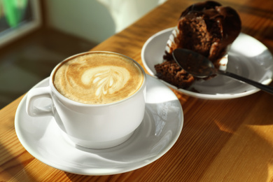 Photo of Cup of fresh aromatic coffee and cupcake at table in cafe