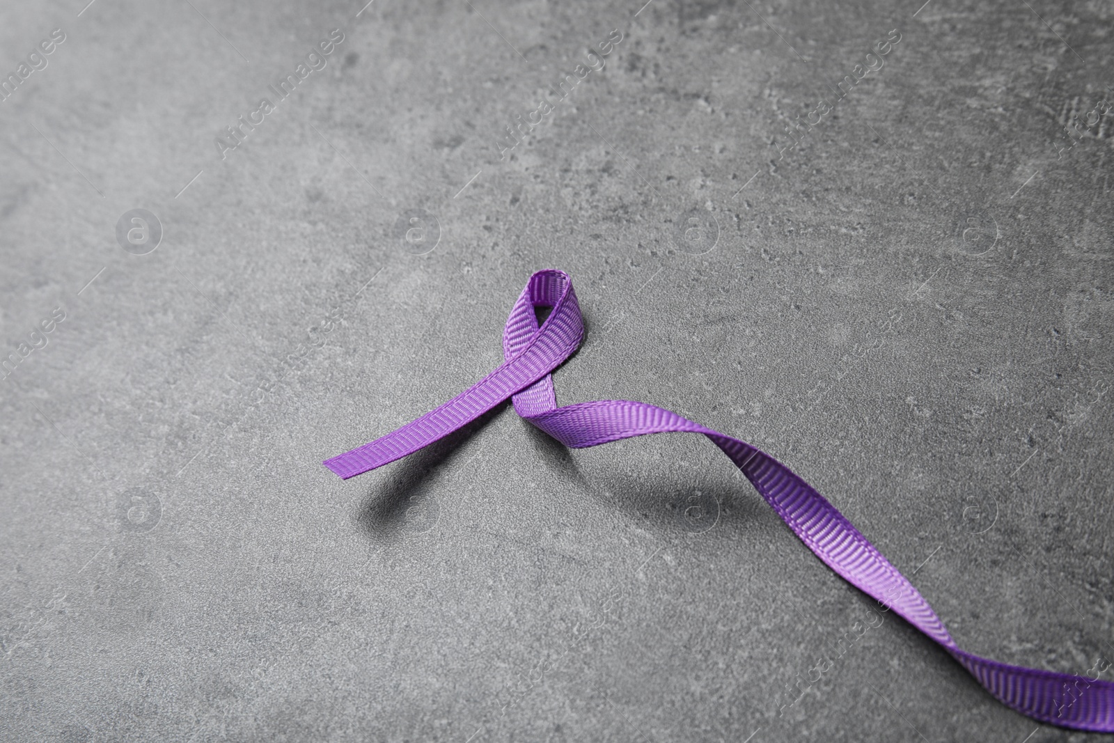 Photo of Purple ribbon on grey stone background, space for text. Domestic violence awareness