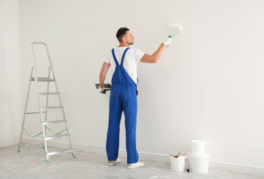 Photo of Man painting wall with white dye indoors