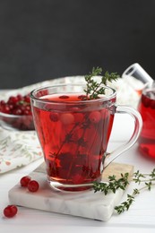 Photo of Tasty hot cranberry tea with thyme and fresh berries in glass cup on white wooden table