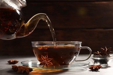 Photo of Pouring aromatic anise tea from teapot into glass cup on light grey table