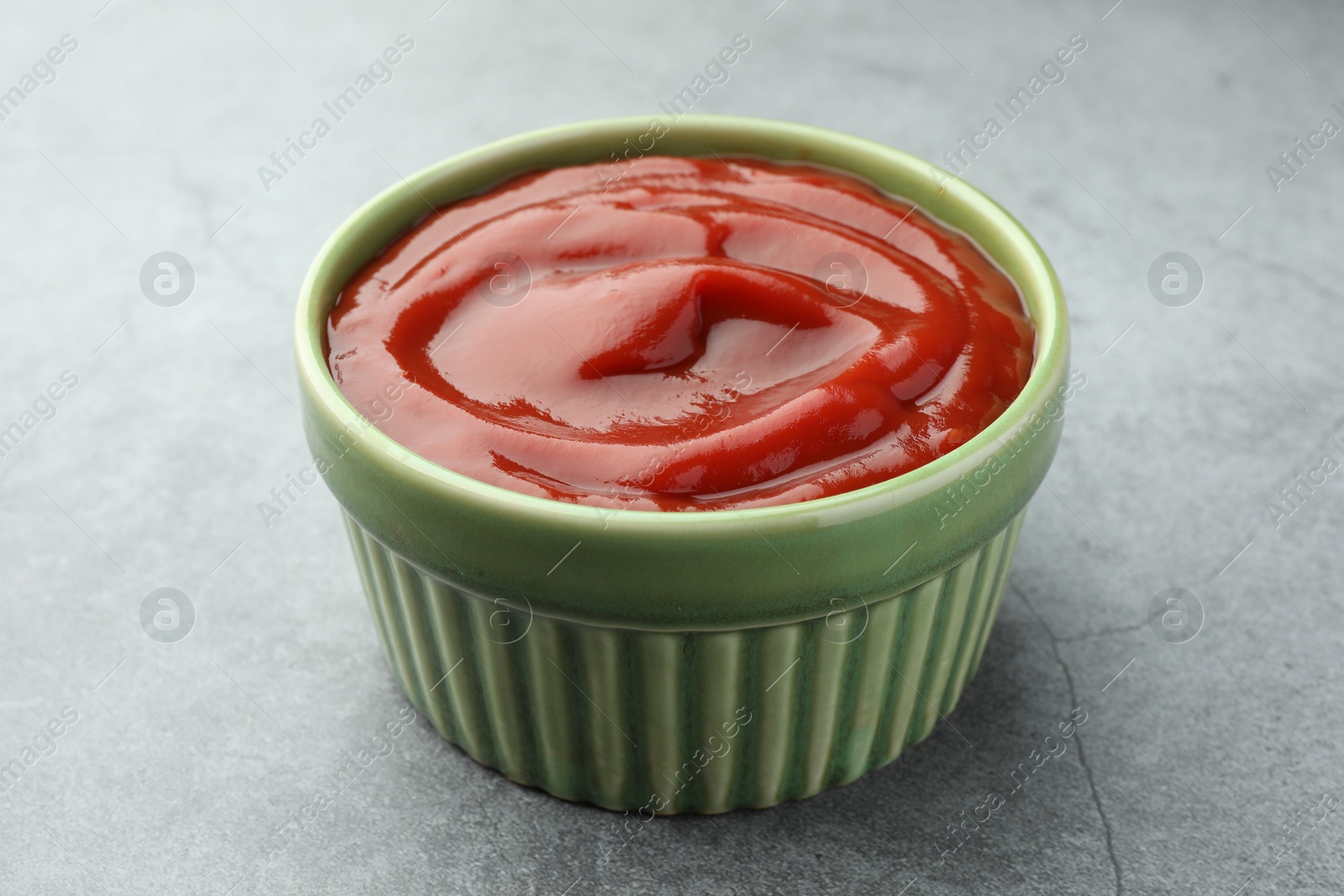 Photo of Bowl of tasty ketchup on light grey table, closeup