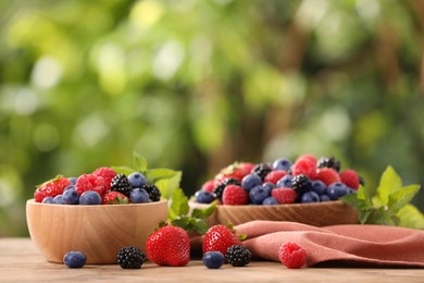 Bowls with different fresh ripe berries and mint on table outdoors