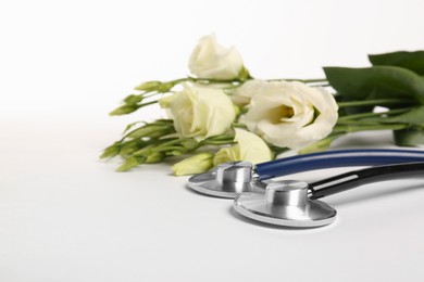 Photo of Stethoscopes and eustoma flowers on white background, closeup. Happy Doctor's Day