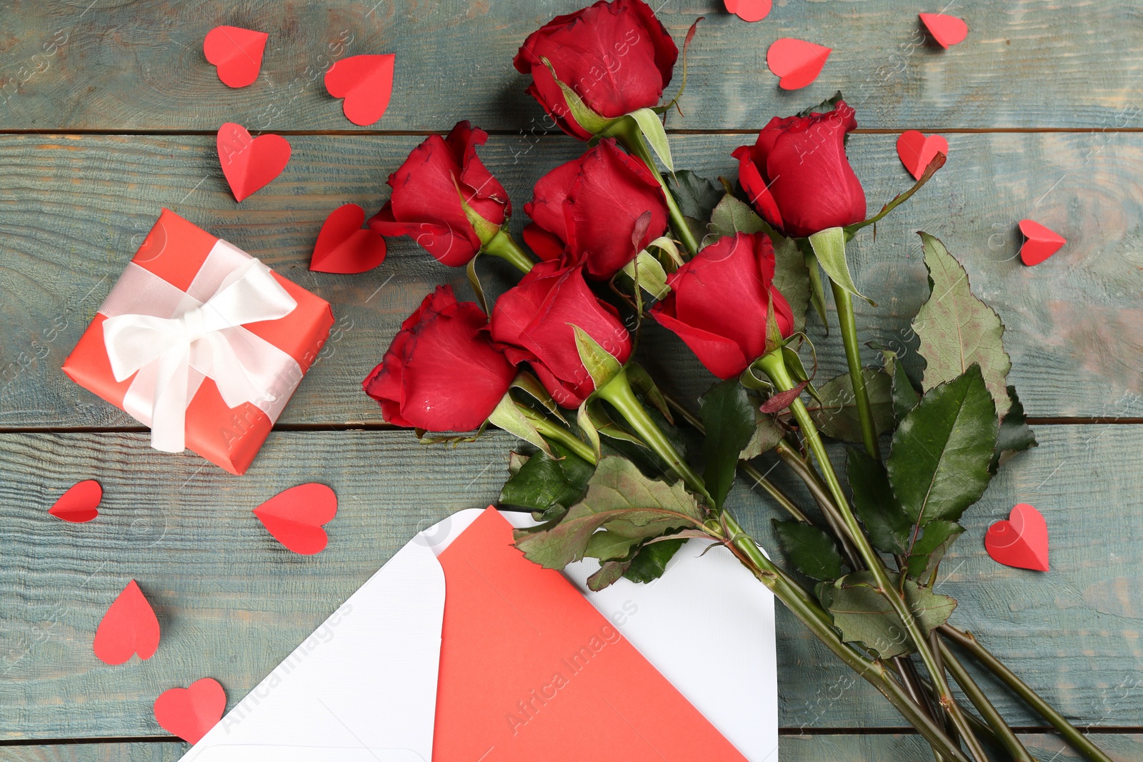 Photo of Flat lay composition with beautiful red roses and gift box on blue wooden background. Valentine's Day celebration