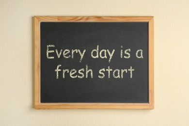 Photo of Small chalkboard with motivational quote Every day is a fresh start on beige background, top view