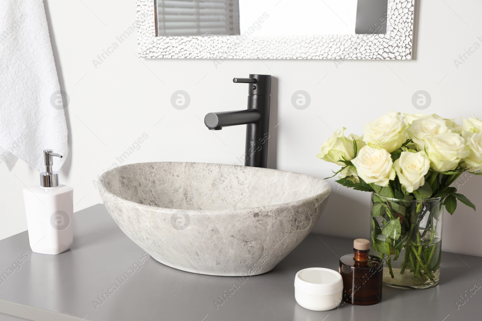 Photo of Vase with beautiful white roses and toiletries near sink in bathroom