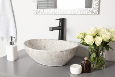 Vase with beautiful white roses and toiletries near sink in bathroom