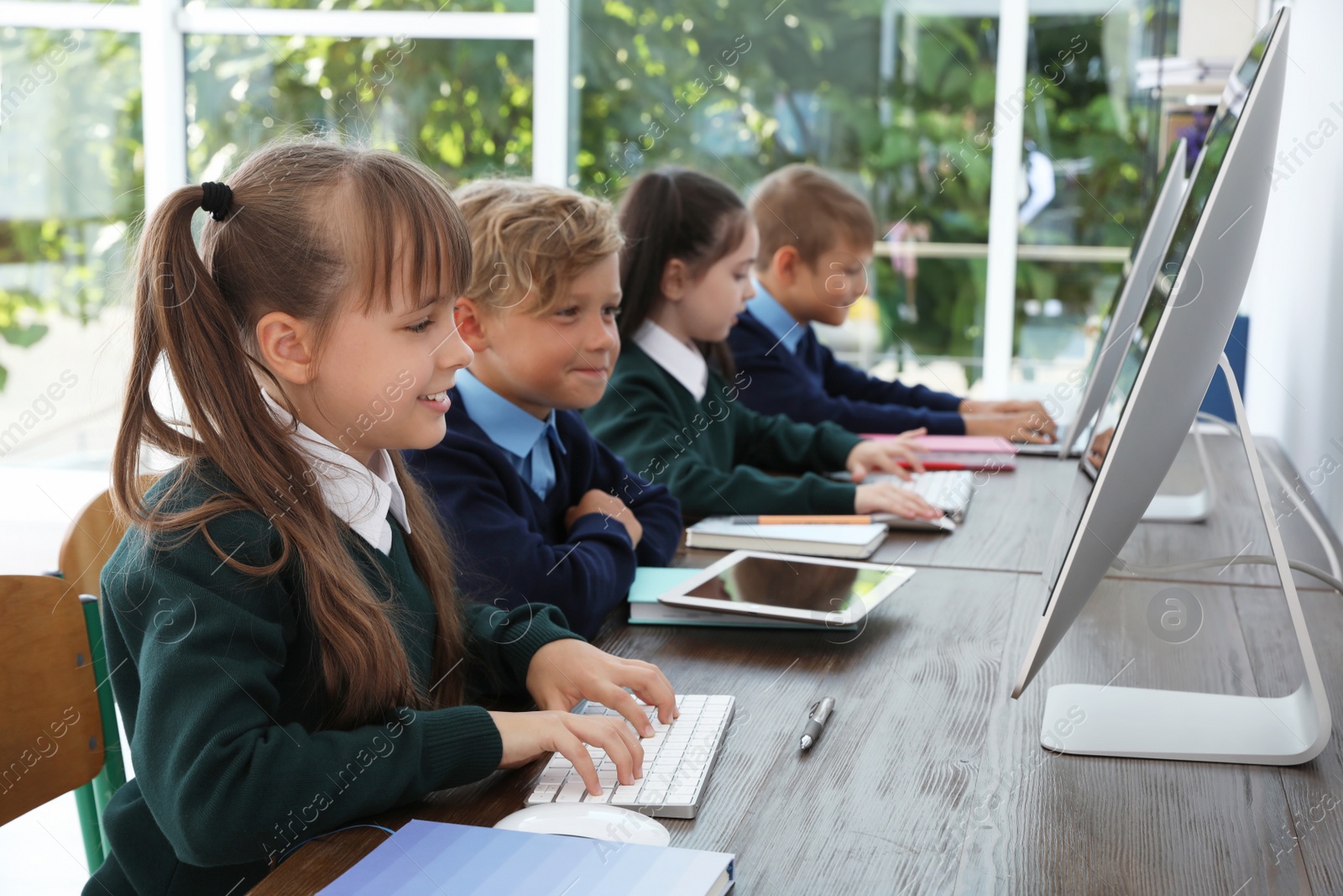 Photo of Little children in stylish school uniform at desks with computers