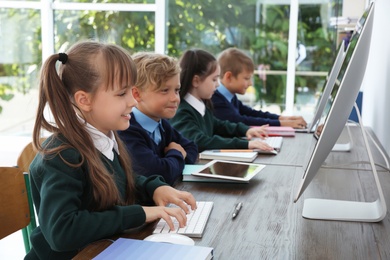 Photo of Little children in stylish school uniform at desks with computers