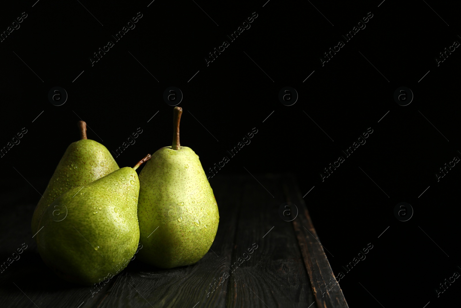 Photo of Ripe pears on wooden table against dark background. Space for text