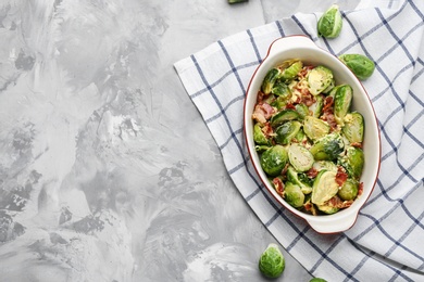 Delicious Brussels sprouts with bacon in baking pan on grey table, top view. Space for text