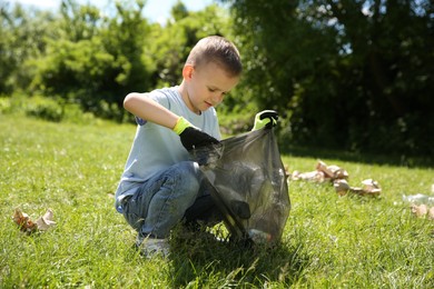 Little boy with plastic bag collecting garbage in park