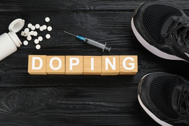 Photo of Cubes with word Doping, sport shoes and drugs on black wooden background, flat lay