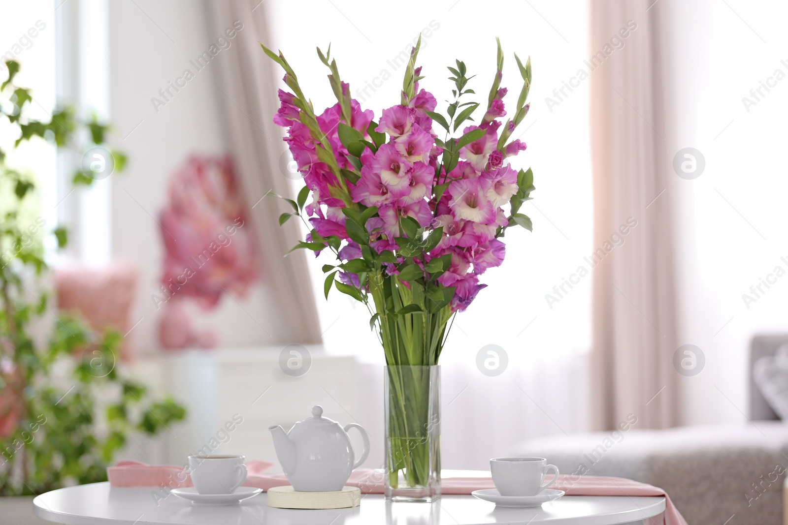 Photo of Vase with beautiful pink gladiolus flowers on wooden table in living room