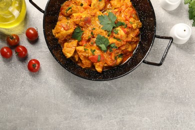 Photo of Delicious chicken curry in frying pan, tomatoes and oil on light grey table, flat lay. Space for text