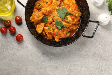 Delicious chicken curry in frying pan, tomatoes and oil on light grey table, flat lay. Space for text