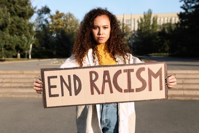 Photo of African American woman holding sign with phrase End Racism outdoors
