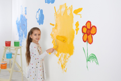 Photo of Little child painting wall with roller brush indoors