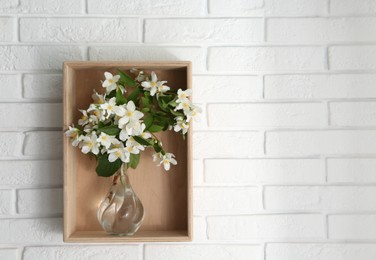 Photo of Wooden shelf with bouquet of beautiful jasmine flowers in vase on white brick wall, space for text