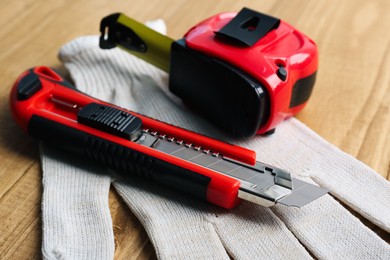 Utility knife, measuring tape and glove on wooden table, closeup