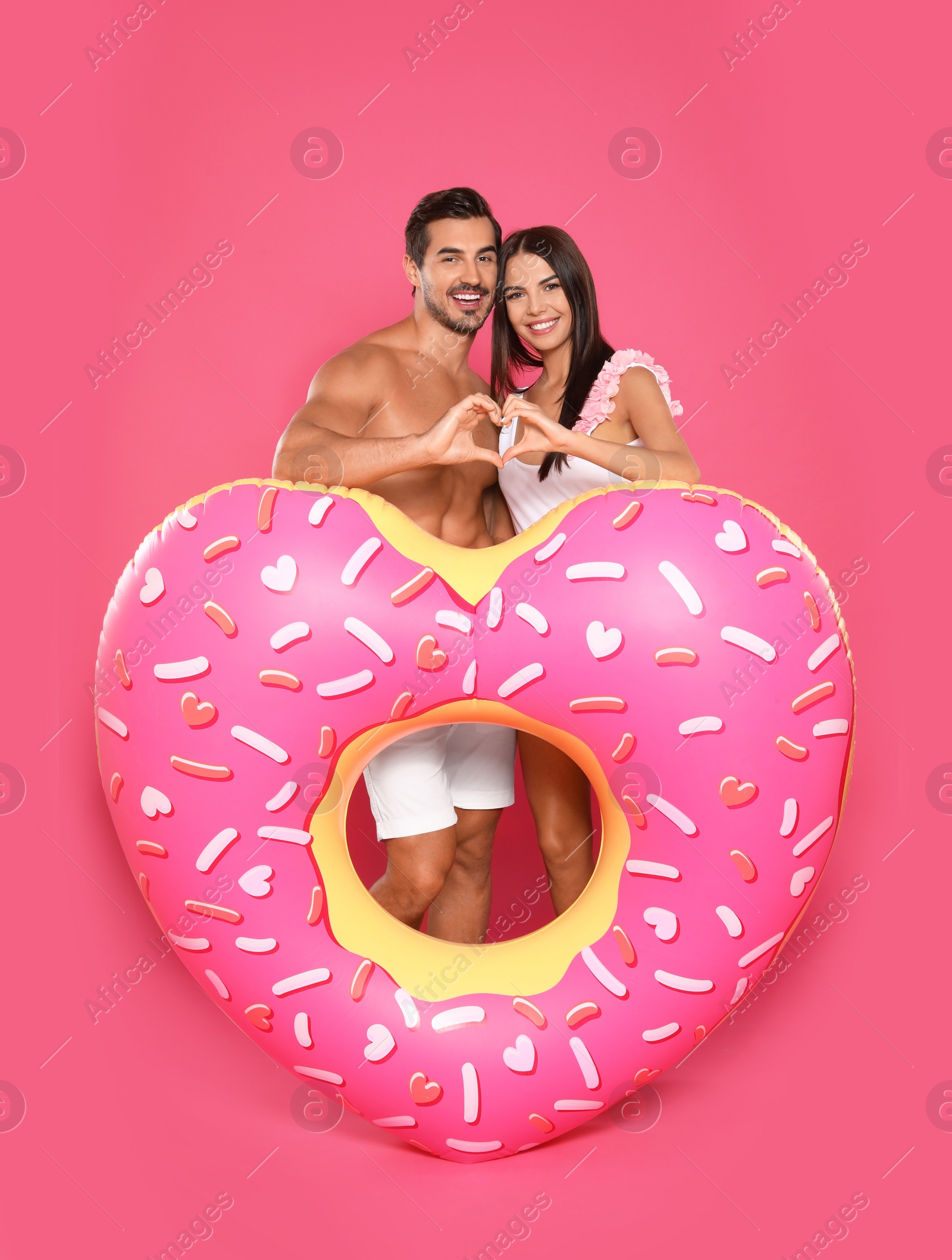 Photo of Young attractive couple in beachwear with inflatable ring on pink background