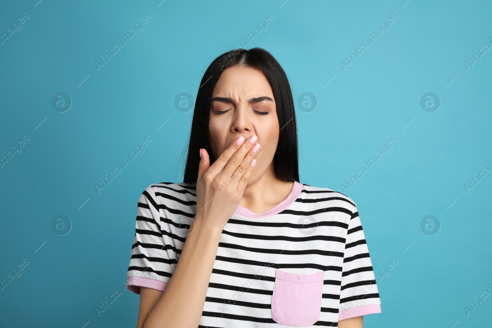 Photo of Young tired woman yawning on light blue background