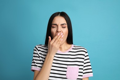 Young tired woman yawning on light blue background