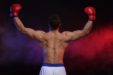 Photo of Man wearing boxing gloves on dark background, back view