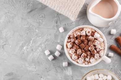 Cup of aromatic hot chocolate with marshmallows, and cocoa powder served on gray table, flat lay. Space for text