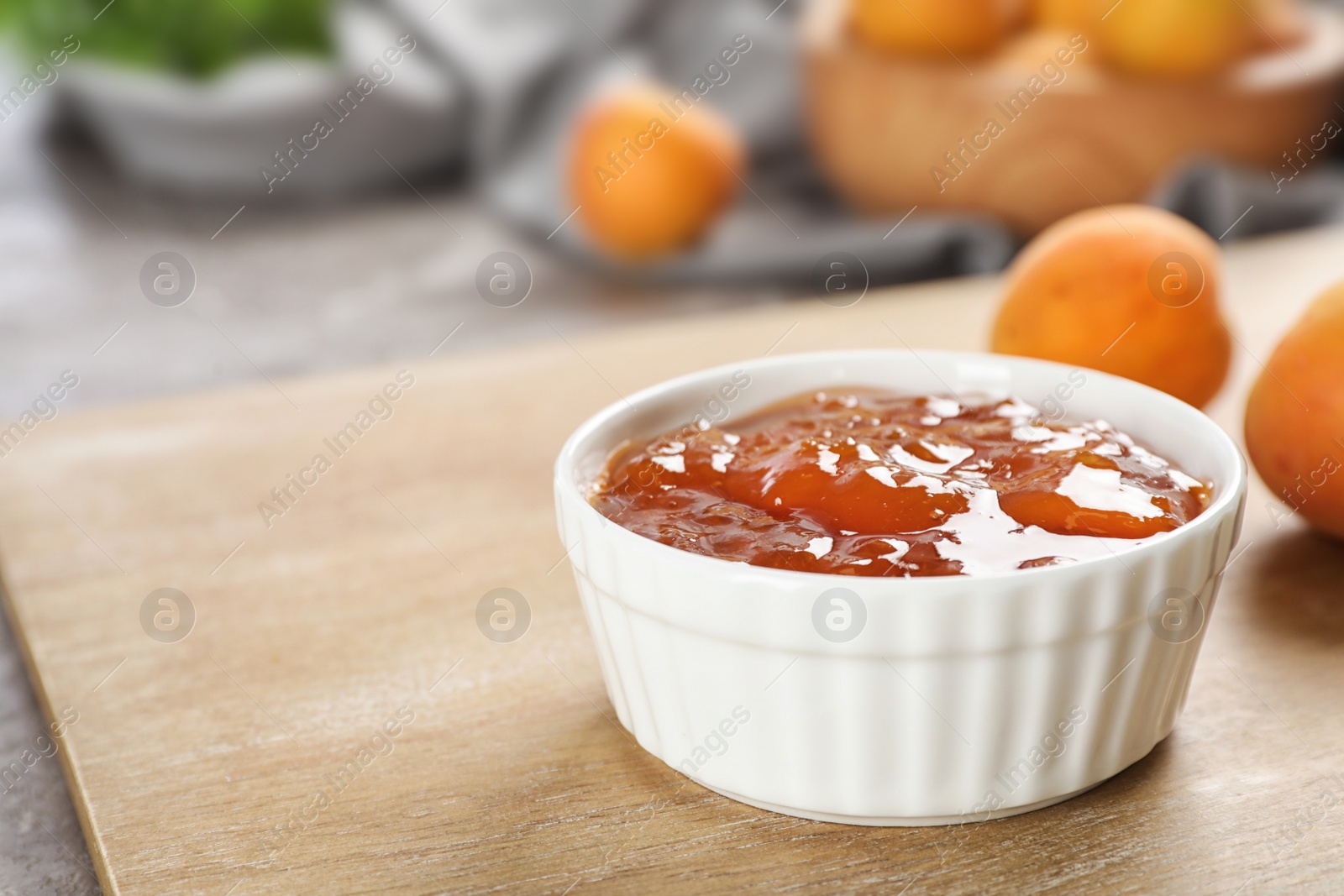 Photo of Bowl with tasty apricot jam on wooden board