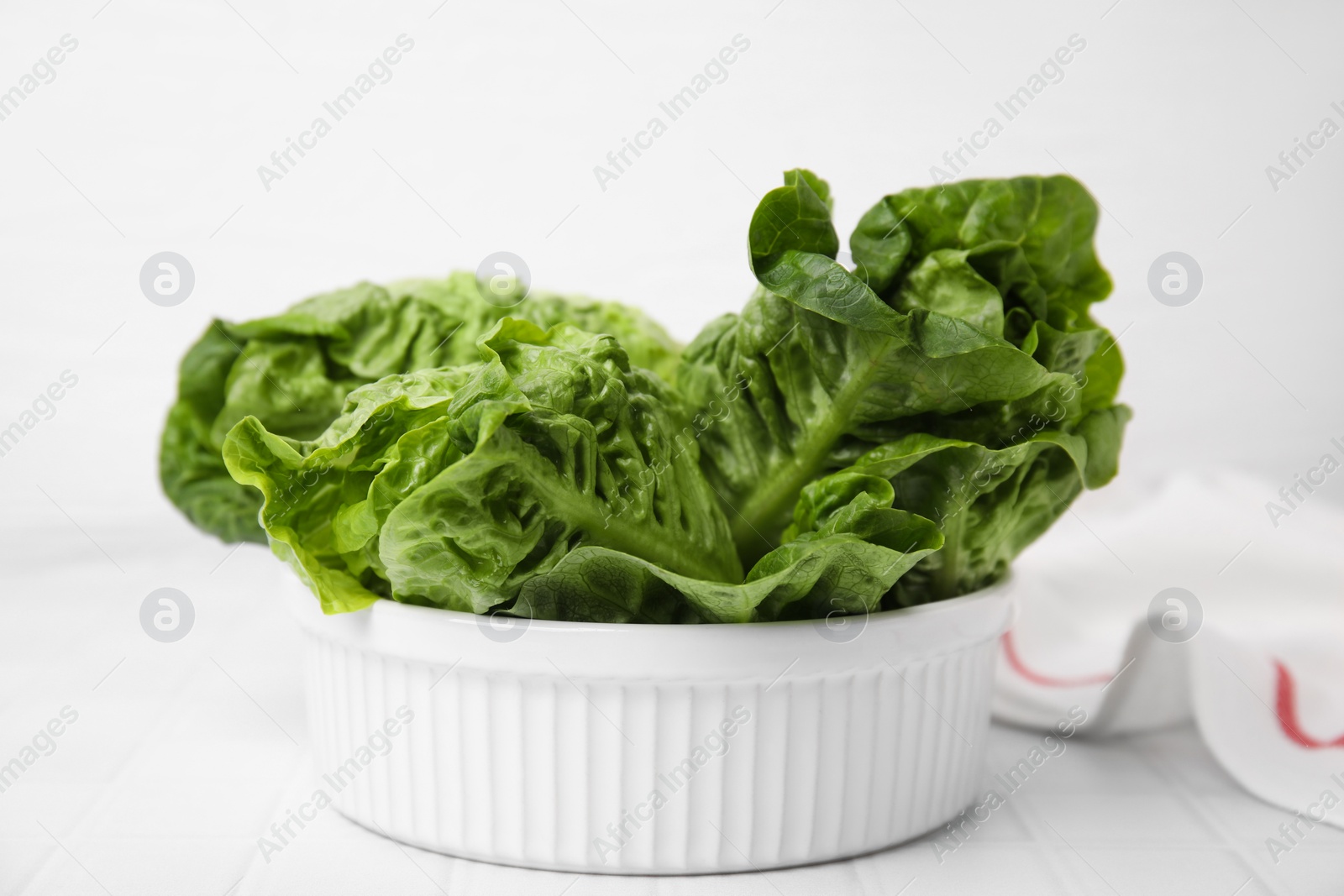 Photo of Bowl with fresh green romaine lettuces on white tiled table