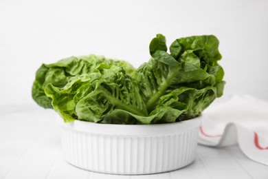 Photo of Bowl with fresh green romaine lettuces on white tiled table