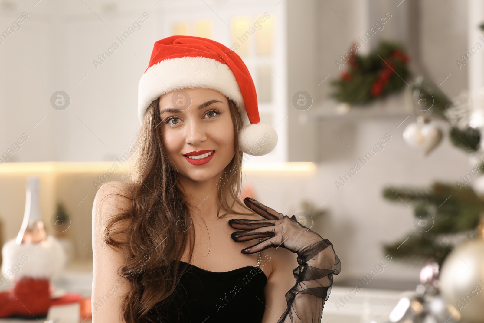 Photo of Beautiful young smiling woman in Santa hat at home, space for text. Celebrating Christmas