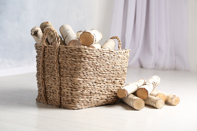 Wicker basket with cut firewood on white floor indoors