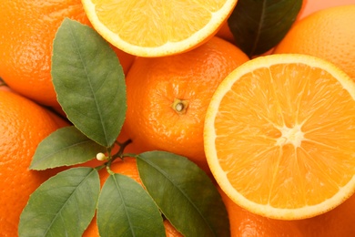 Cut and whole fresh ripe oranges with green leaves as background, top view