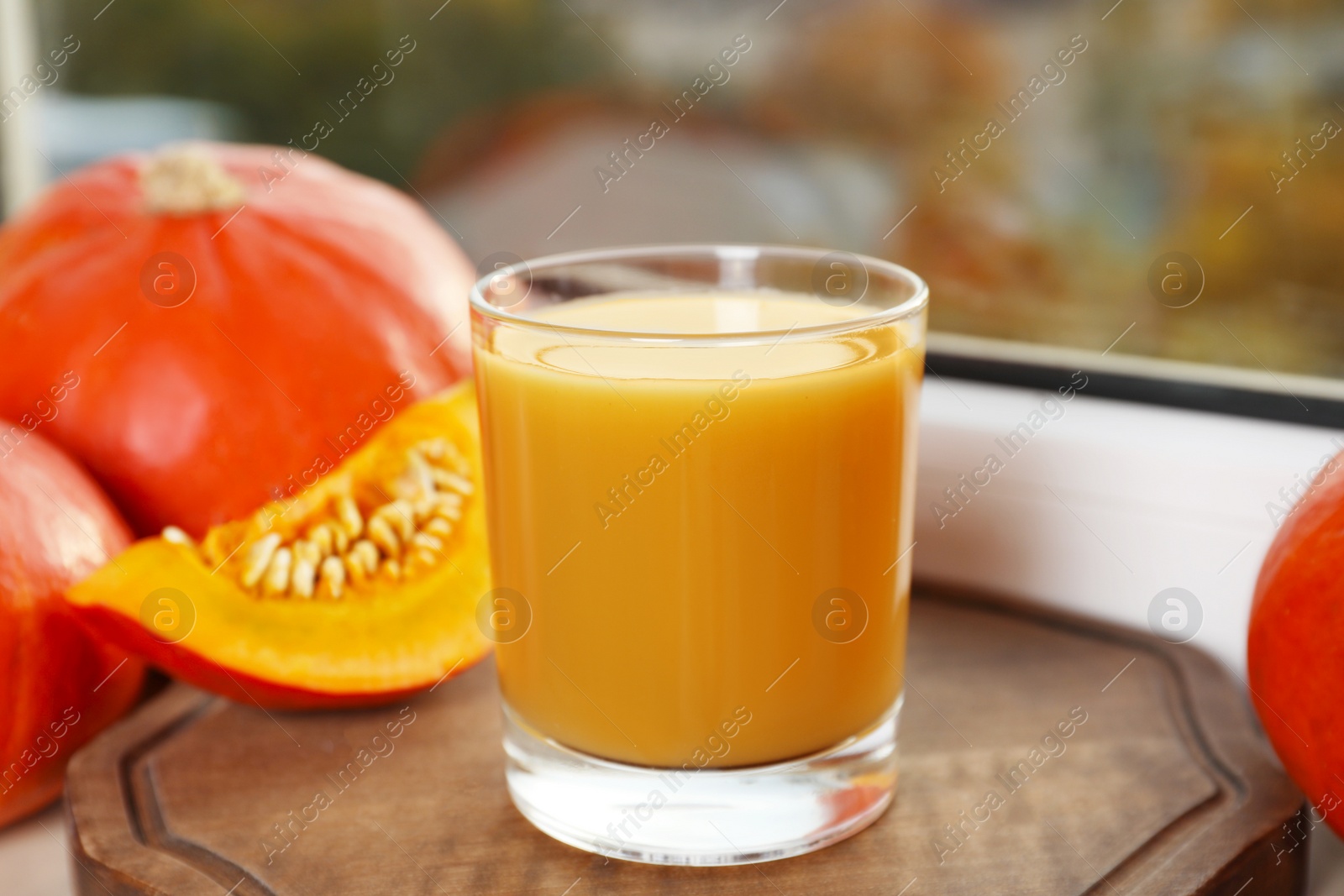 Photo of Tasty pumpkin juice in glass, whole and cut pumpkins on windowsill indoors