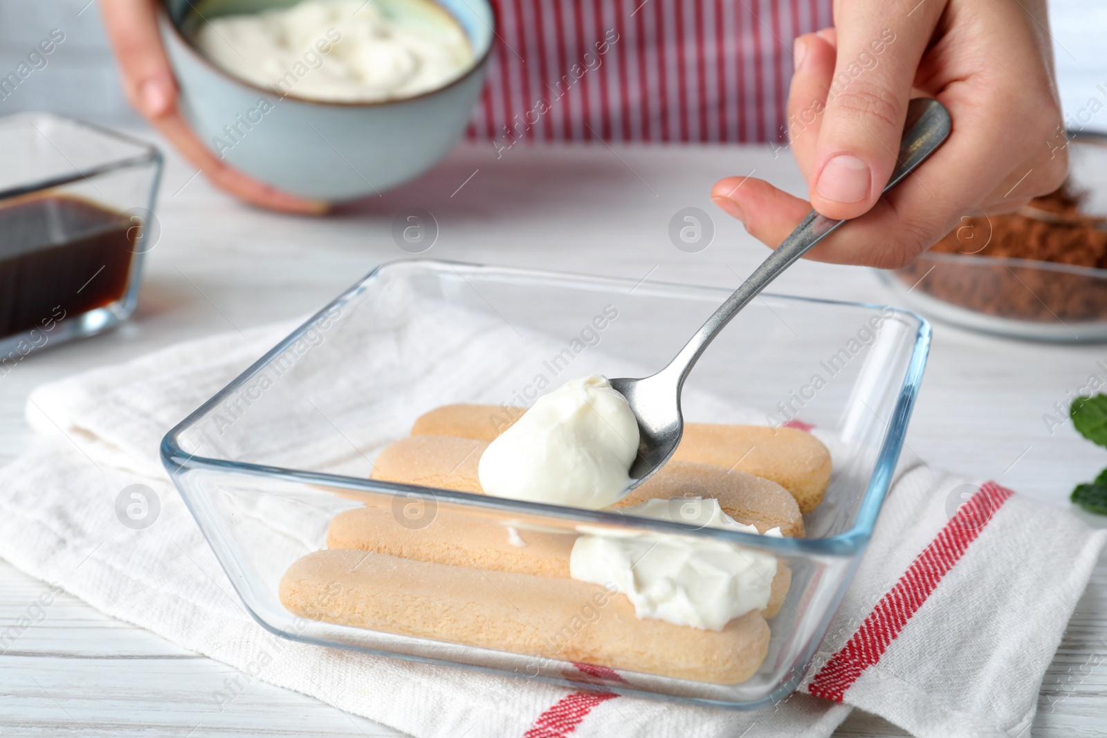 Photo of Woman making tiramisu cake at white wooden table, closeup