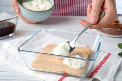 Woman making tiramisu cake at white wooden table, closeup