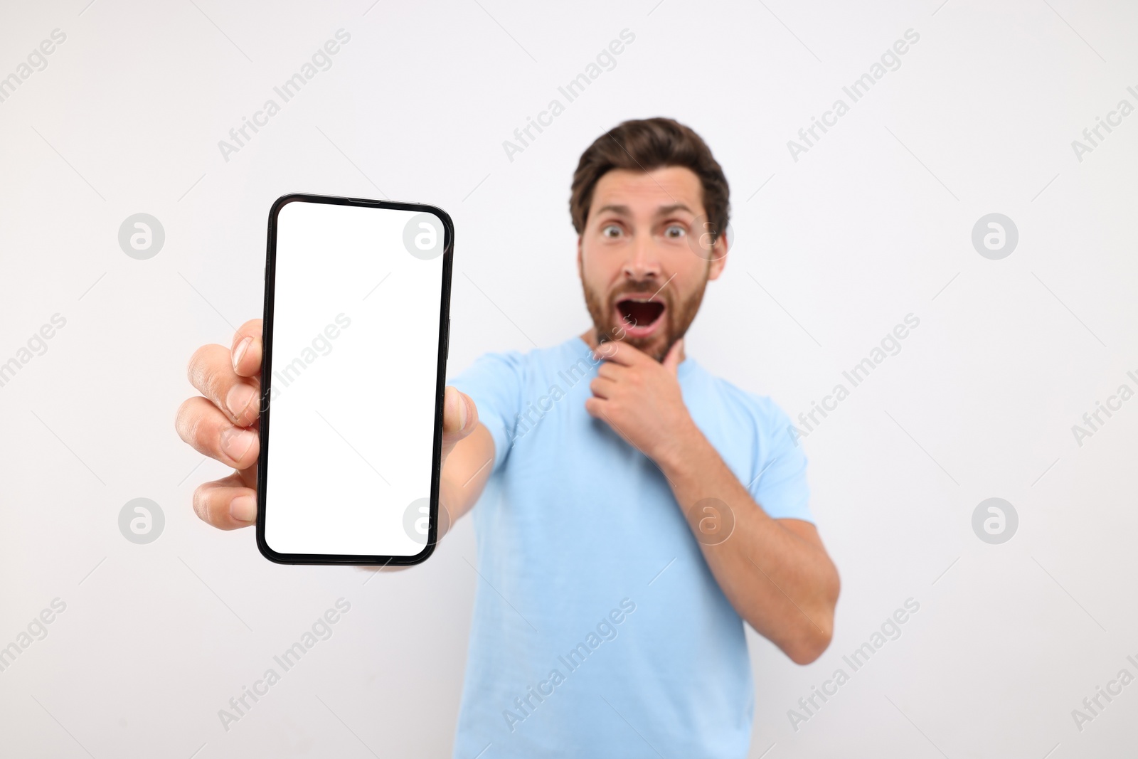 Photo of Surprised man showing smartphone in hand on white background, selective focus. Mockup for design