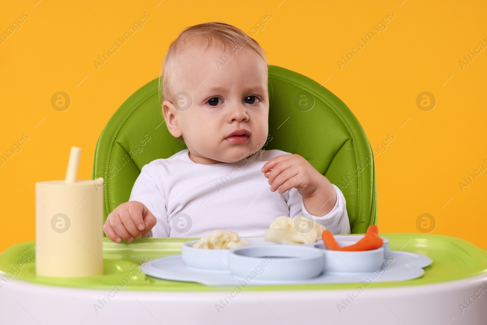 Photo of Cute little baby with healthy food in high chair on orange background