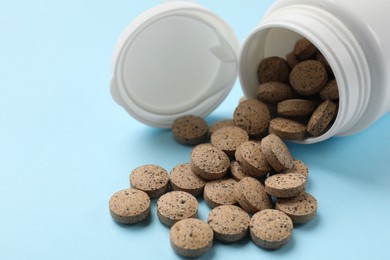 Photo of Bottle and vitamin pills on light blue background, closeup