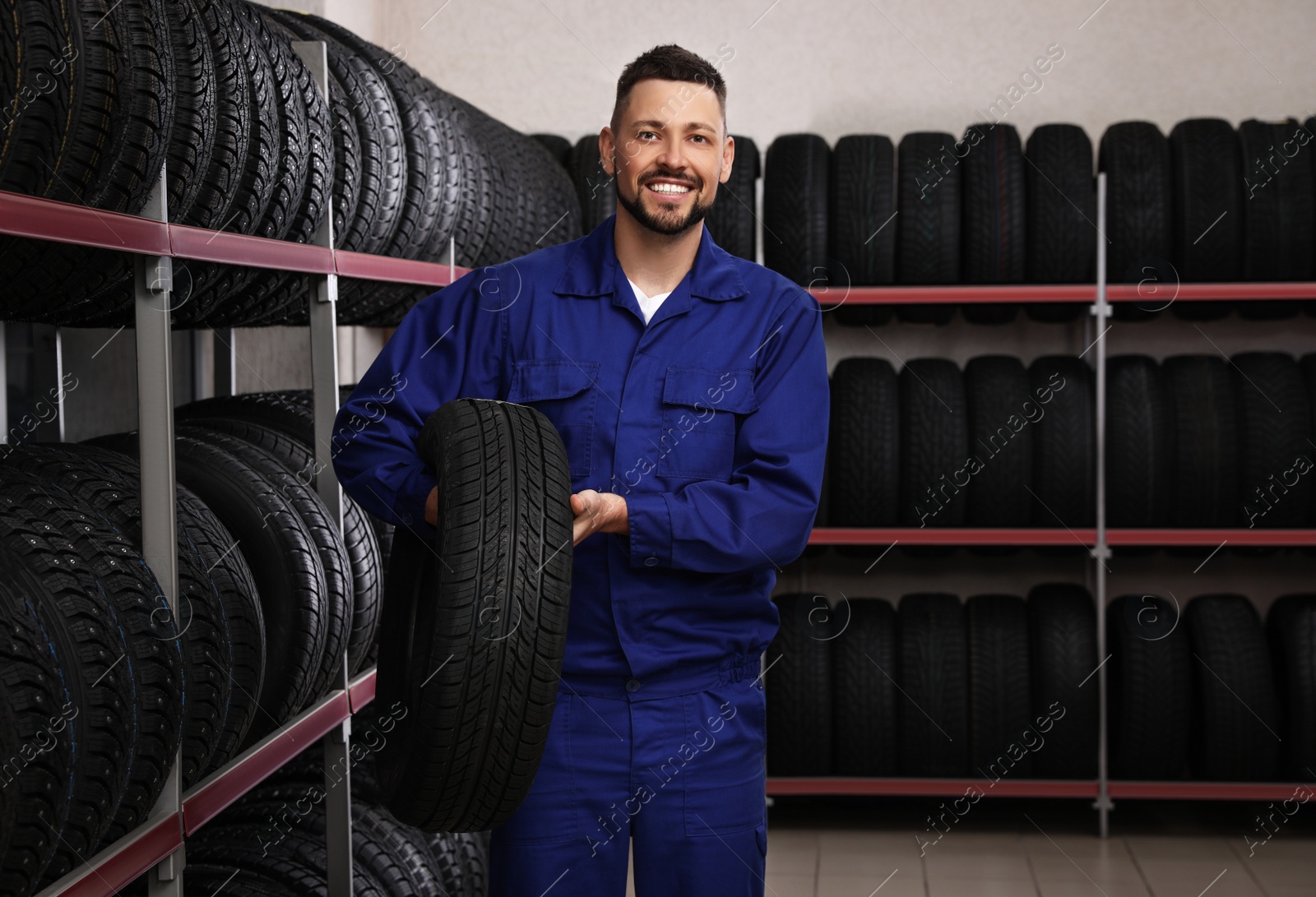 Photo of Male mechanic with car tire in auto store