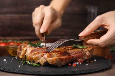 Photo of Woman eating delicious fried meat with rosemary and spices at table, closeup