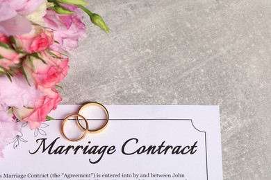 Marriage contract, golden wedding rings and flowers on grey table, above view