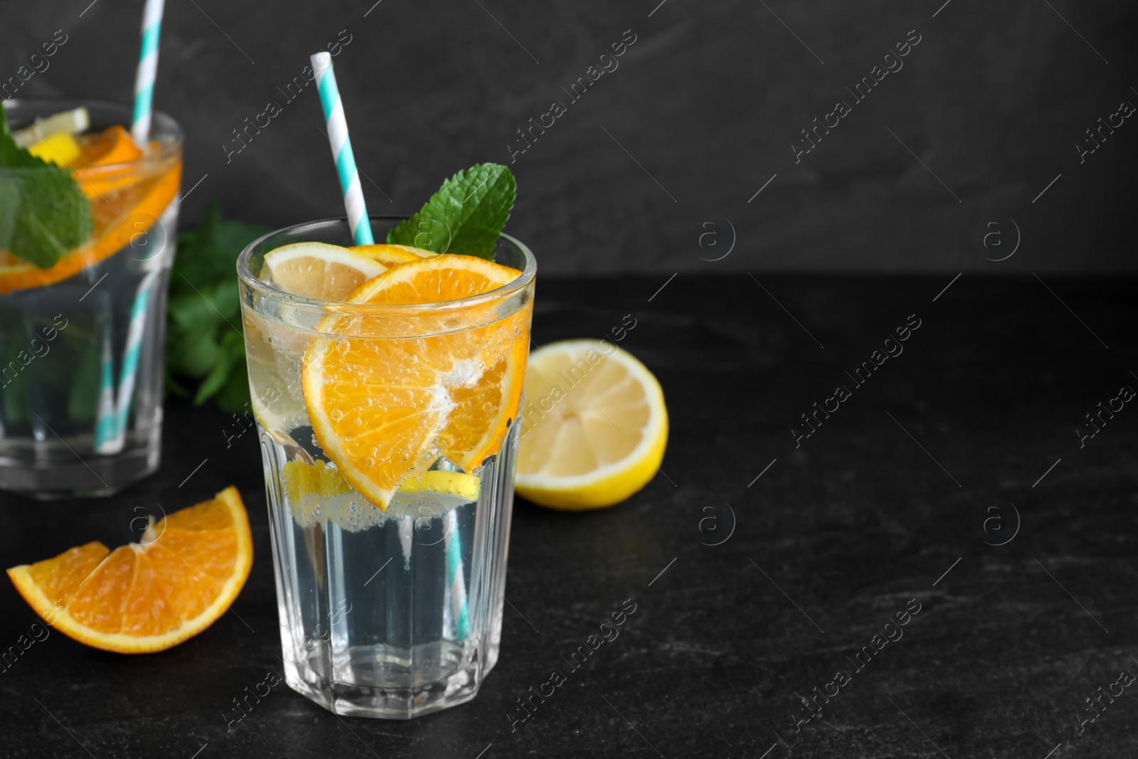 Photo of Delicious orange lemonade with soda water and mint on black table, space for text. Fresh summer cocktail