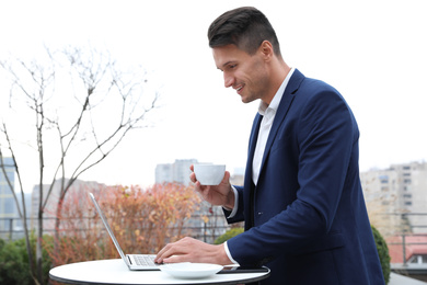 Photo of Businessman with laptop and coffee in outdoor cafe. Corporate blog